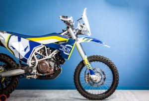 Moderne Husqvarna Enduro-Motorrad in auffälligem Design vor blauem Hintergrund, ideal für Offroad-Abenteuer und erhältlich bei Bräuer Motorradsport KG.