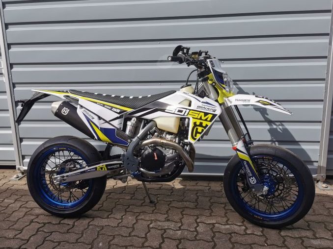 Husqvarna 701 SM Supermoto Motorrad in modernem Design mit gelben und blauen Akzenten, ausgestellt vor einer grauen Wand.