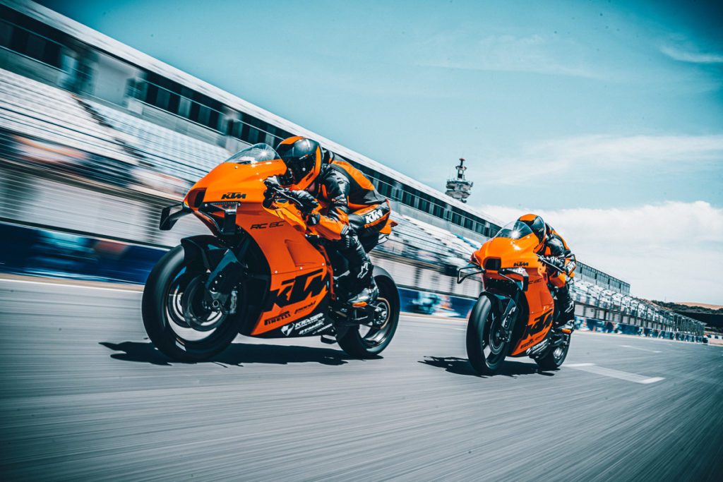 Zwei KTM-Rennmotorräder fahren schnell auf einer Rennstrecke und zeigen sportliches Design und Leistung.