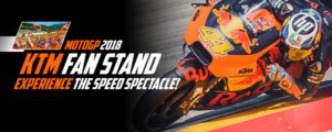 Motorradfahrer auf einer KTM beim MotoGP-Rennen 2018, umgeben von begeisterten Fans im KTM Fan Stand.