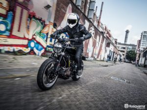 Ein Motorradfahrer in Schutzkleidung fährt auf einer Husqvarna durch eine urban gestaltete Straße mit Graffiti.
